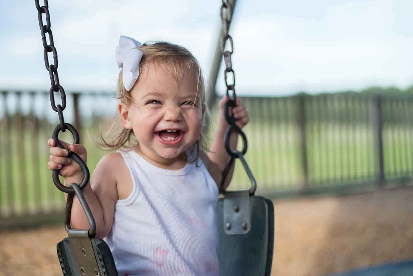 Little girl smiling and laughing while swinging on playset at park