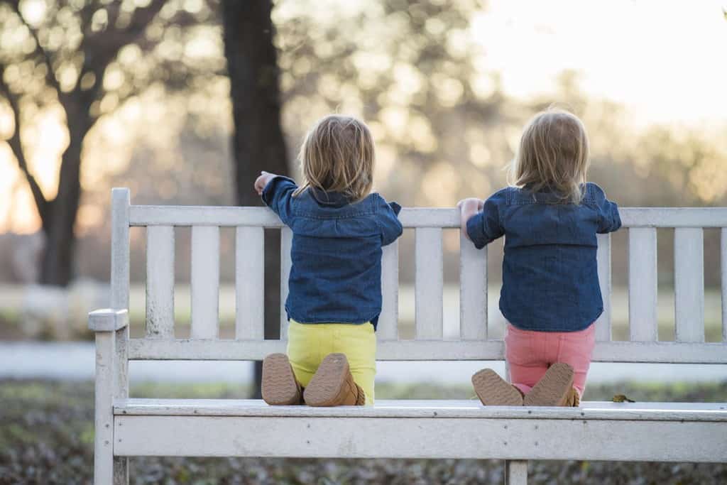 Two little girls sitting backwards on bench at park