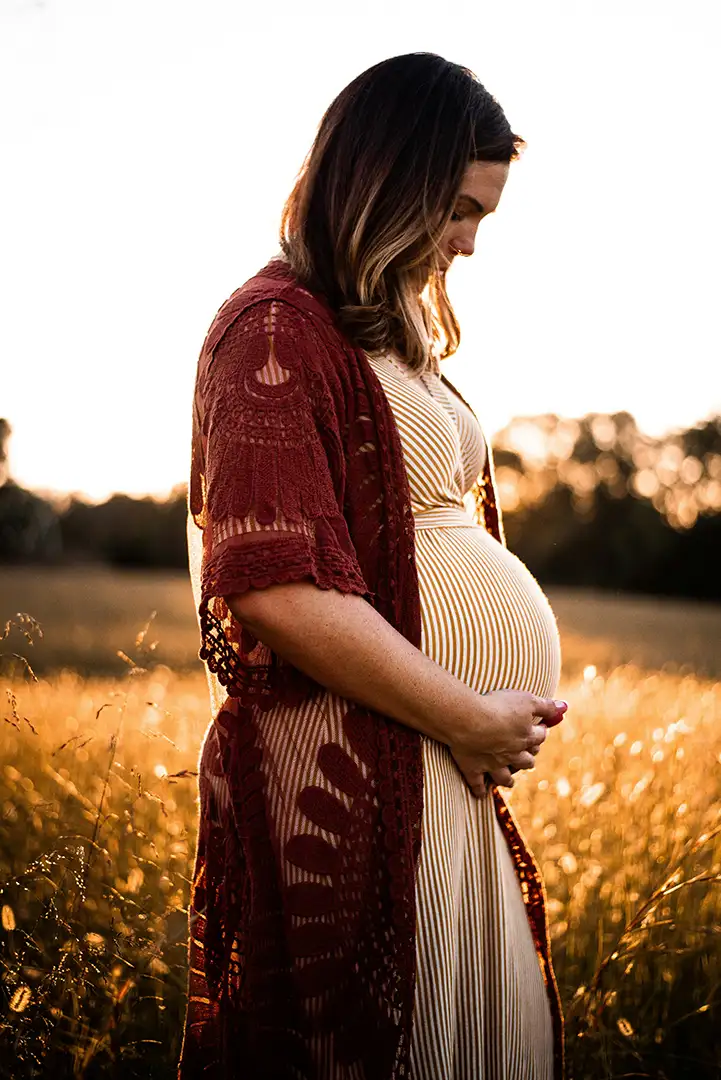 Pregnant mother in fall field lovingly holding belly