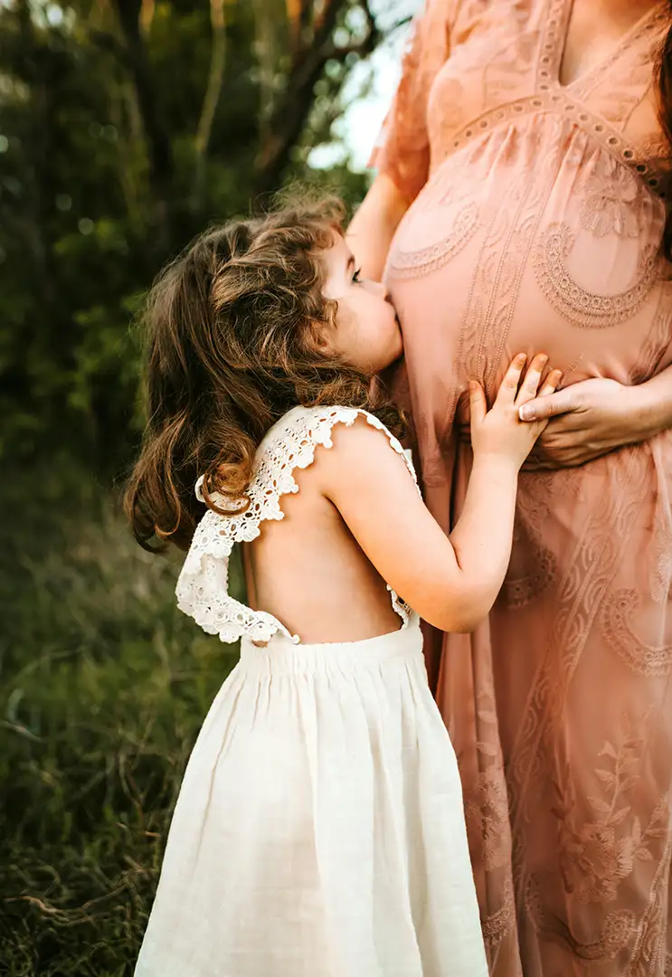 Young girl kissing belly of pregnant mother