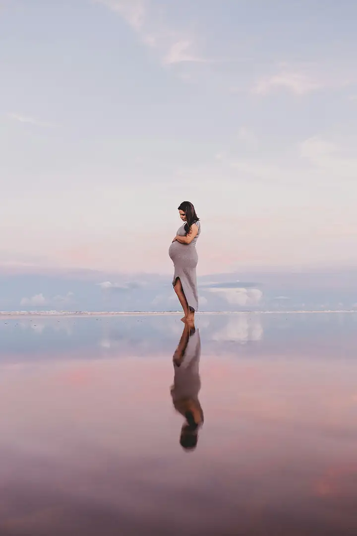 Pregnant woman standing serenely in shallow, reflective water