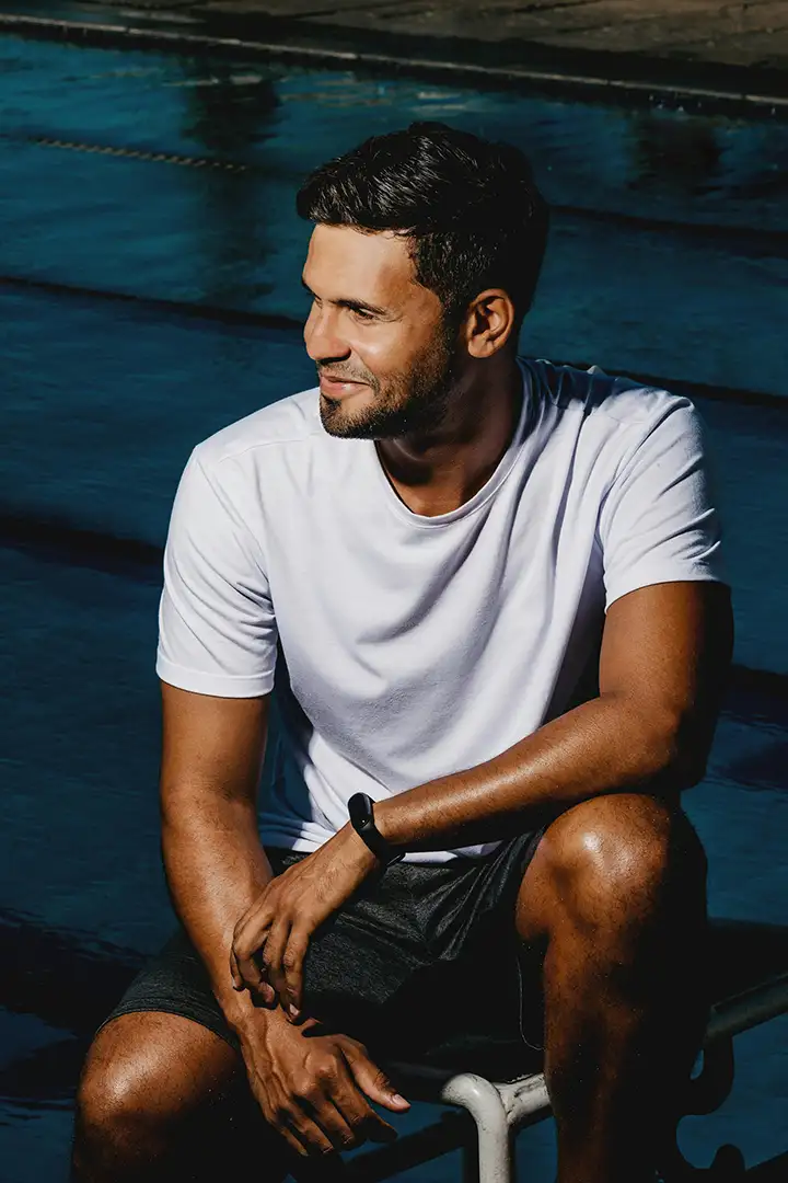 A cheerful, muscular man sitting poolside in summer sunlight, embodying leisure and confidence
