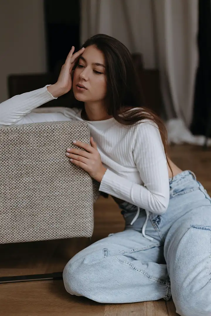 Woman suffering from chronic pain leaning against couch