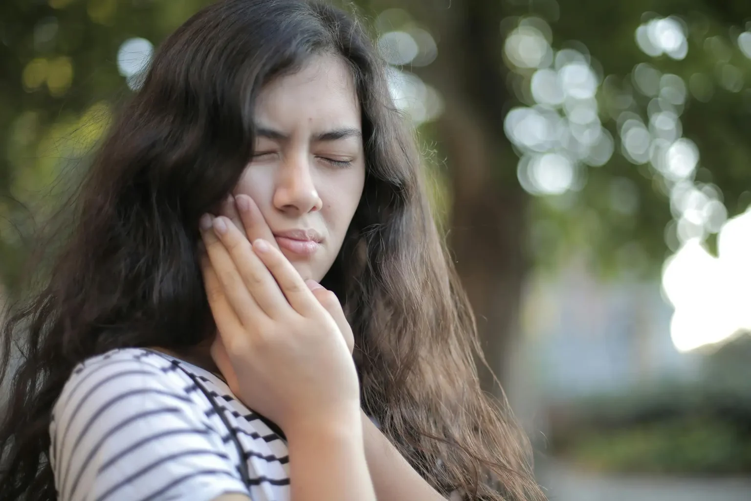 Portrait of a young woman feeling toothache, showing discomfort outdoors with a pained facial expression