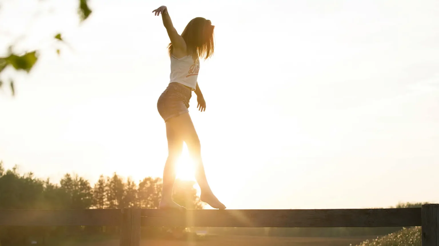 A young woman balancing on a fence during a serene sunrise, exuding freedom and joy