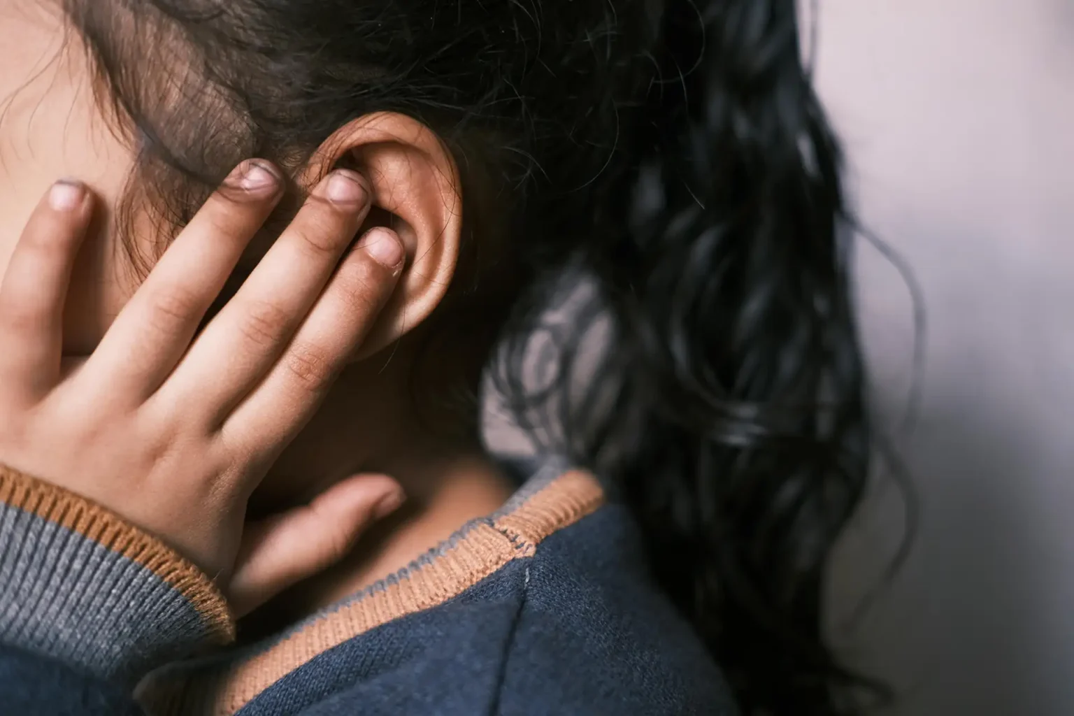 A young girl with long dark hair covering her ear in a thoughtful pose