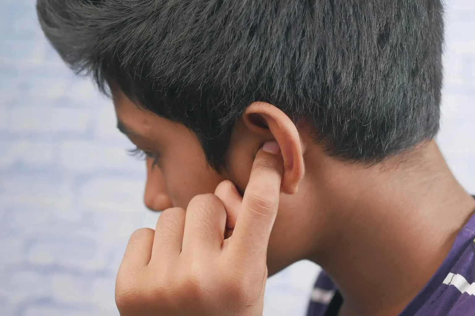 Close-up of a teenager's profile with hand covering ear, reflecting introspection, concentration, or discomfort