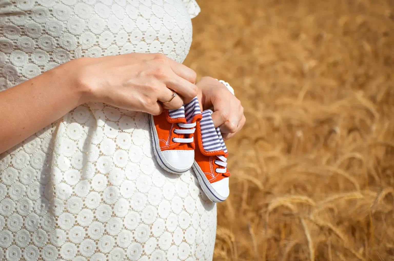 Pregnant woman holding tiny red baby shoes over her belly