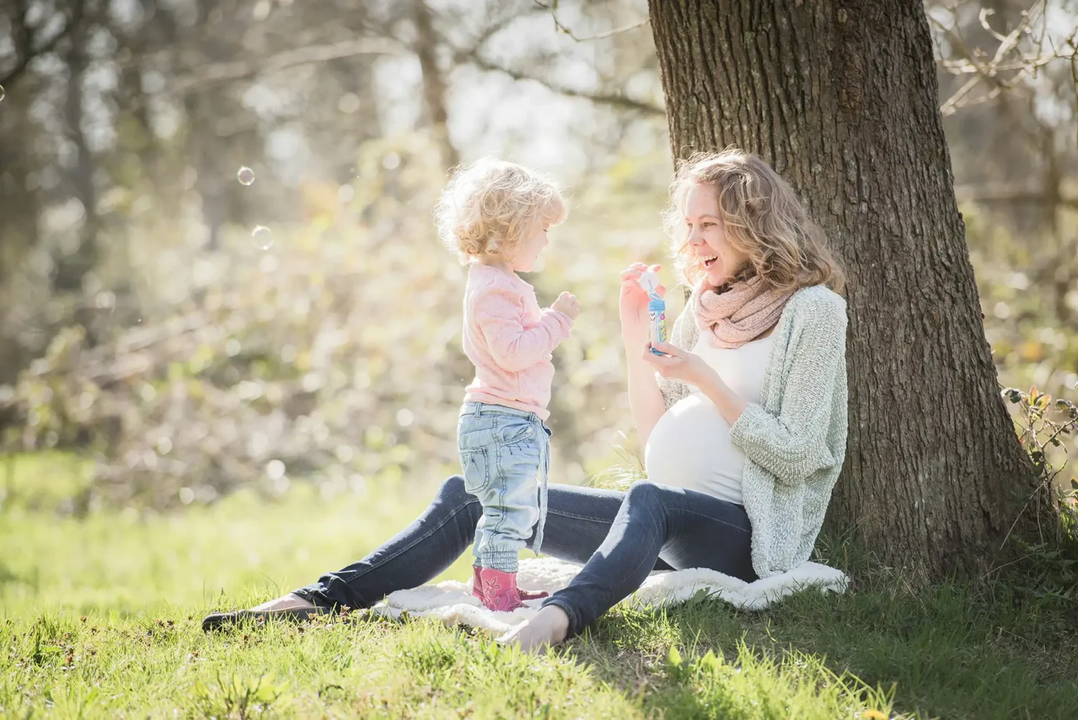 Pregnant mother playing with child while sitting by tree