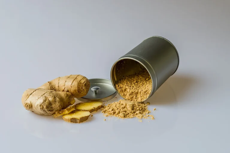 Close-up of fresh ginger root with sliced pieces and ginger powder spilled from a metal container