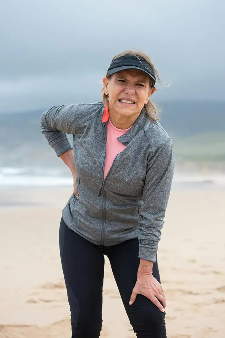 Woman on beach leaning over in pain