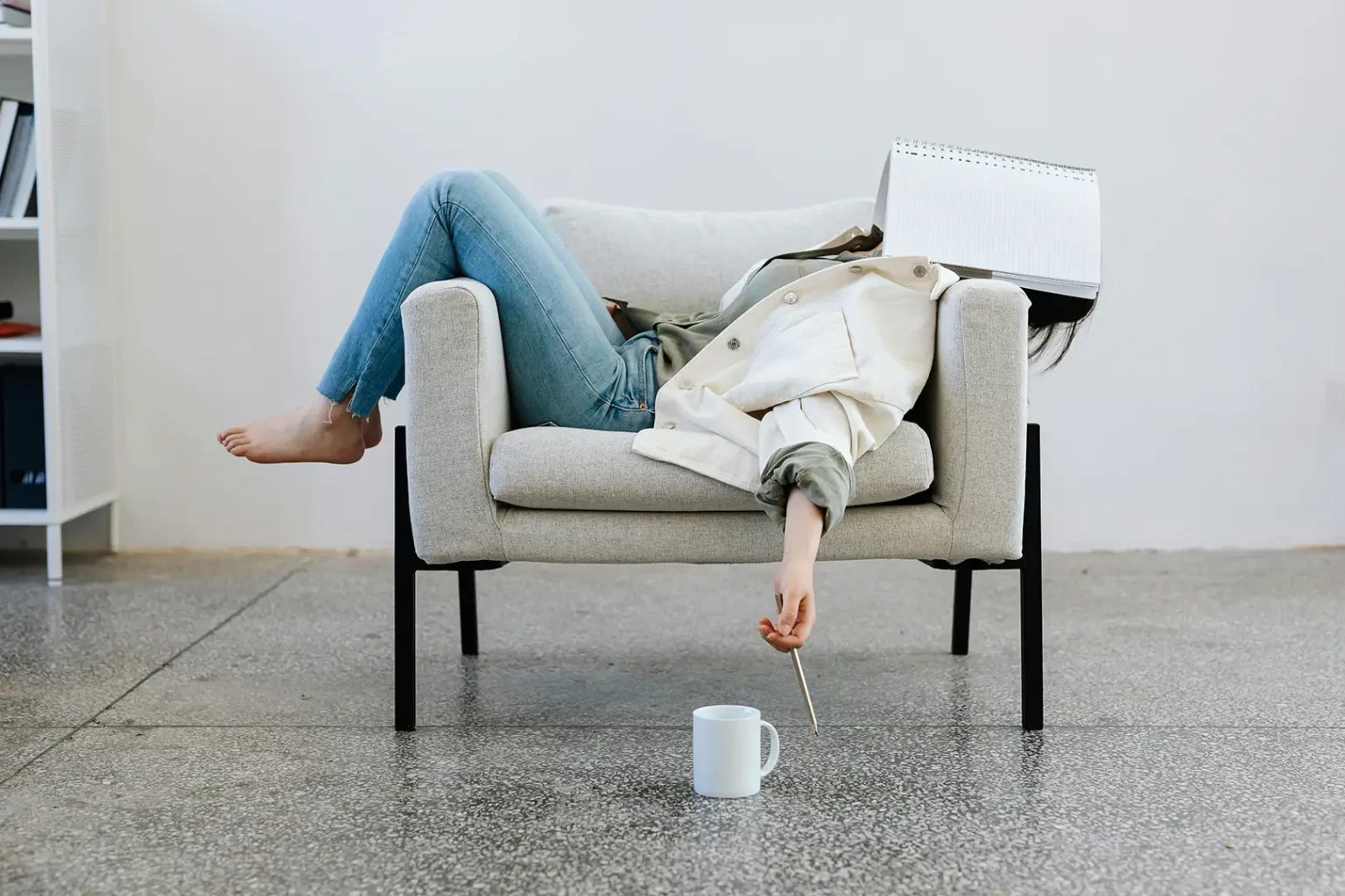 Stressed woman laying on couch with notebook over face.